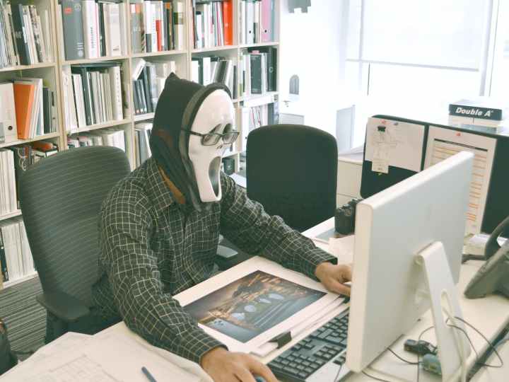 person wearing scream mask and black dress shirt while facing computer table during daytime